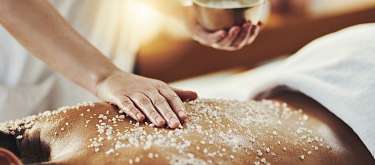 Hand streut Meersalz auf den Rücken während einer Spa-Massage, achtsame Berührung und tiefe Entspannung I WUNDERORTE