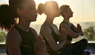 Wundervolle spirituelle Stimmung, junge, moderne Frauen meditieren im Lotussitz während des Sonnenuntergang am Strand eines Wellness Hotel