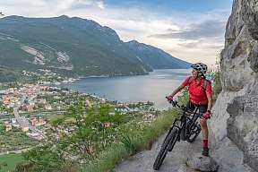 Mountainbikerin auf schmalem Pfad oberhalb von Torbole mit weitem Blick über den Gardasee – sportlicher Aktivurlaub in Italien I WUNDERORTE