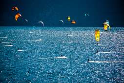 Zahlreiche Kitesurfer gleiten bei kräftigem Wind über den Gardasee nahe Torbole – beliebter Spot für Aktivurlaub und Wassersport in Italien I WUNDERORTE