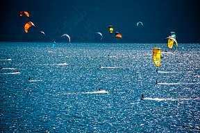 Zahlreiche Kitesurfer gleiten bei kräftigem Wind über den Gardasee nahe Torbole – beliebter Spot für Aktivurlaub und Wassersport in Italien I WUNDERORTE