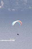 Tandem-Paraglider schwebt über dem Gardasee mit Blick auf Ausflugsschiff und bewaldete Ufer – ideal für Sport- und Abenteuerurlaub in Italien I WUNDERORTE