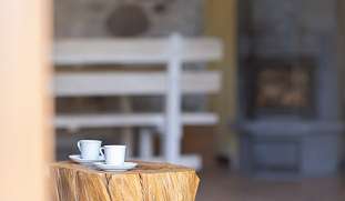 Zwei Espressotassen auf einem Tisch aus Baumstamm im Wohnzimmer mit Kamin – ruhiger Moment im Landhaus bei Arco am Gardasee I WUNDERORTE