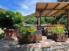 Überdachte Terrasse mit Holzbänken, Natursteinmauer und farbenfrohen Blumenkästen inmitten grüner Berglandschaft bei Arco am Gardasee I WUNDERORTE