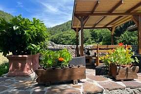 Überdachte Terrasse mit Holzbänken, Natursteinmauer und farbenfrohen Blumenkästen inmitten grüner Berglandschaft bei Arco am Gardasee I WUNDERORTE