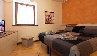 Schlafzimmer mit Doppelbett, gefaltetem Handtuchset, Holzfußboden, Kommode und TV – gemütlicher Rückzugsort im Berghaus bei Arco am Gardasee I WUNDERORTE