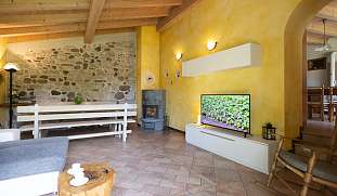 Heller Wohnbereich mit Natursteinwand, Sofa, Kamin, Fernseher und großem Esstisch im Berghaus nahe Arco am Gardasee I WUNDERORT