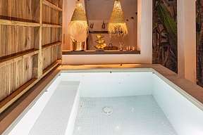 Beleuchteter Pool bei Nacht mit überdachtem Lounge-Bereich &amp; dekorativen Lampen aus Bast