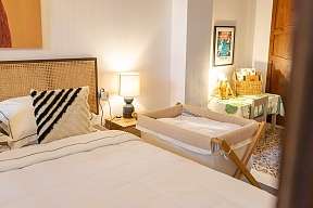 Helles Schlafzimmer mit king size Bett und Baby Beistell-Bett, Nachttischlampe auf Holz-Nachttisch 