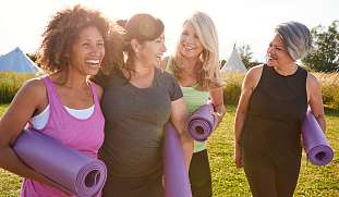 Gruppe lachender Frauen mit Yogamatten auf dem Weg zu einem gemeinsamen Yogakurs in einem Retreat von Wunderorte