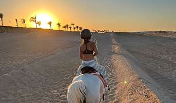 Sporthotel in Ägypten: ein Mädchen das im Sonnenuntergang in der Wüste von Ägypten reitet.