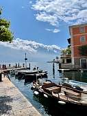 Kleiner Hafen am Gardasee mit traditionellen Holzbooten, Altbauten und beeindruckendem Blick auf die schneebedeckten Alpen I WUNDERORTE