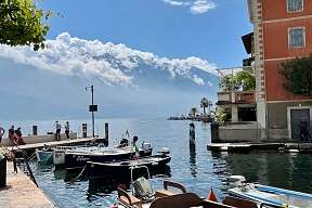 Kleiner Hafen am Gardasee mit traditionellen Holzbooten, Altbauten und beeindruckendem Blick auf die schneebedeckten Alpen I WUNDERORTE
