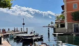 Kleiner Hafen am Gardasee mit traditionellen Holzbooten, Altbauten und beeindruckendem Blick auf die schneebedeckten Alpen I WUNDERORTE