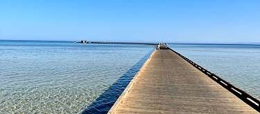 Langer Holzsteg führt über kristallklares Wasser ins offene Meer unter wolkenlosem Himmel – Symbol für Ruhe, Klarheit und Aufbruch bei WUNDERORTE