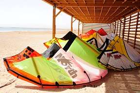 Kites unter Holzüberdachung am Strand in Soma Bay – bunte Ausrüstung für Kitesurfurlaub in Ägypten