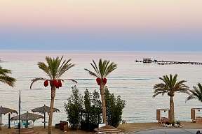Blick vom Strandhotel auf Palmen, Himmel in Pastell und Holzsteg am Roten Meer – The Breakers