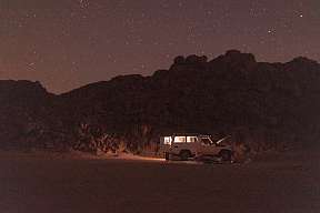 Sternenklare Nacht in der arabischen Wüste mit beleuchtetem Jeep und Campfeuer – unvergessliche Nacht im Wüstencamp