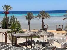 Blick auf Strandlounge mit weißen Sesseln, Palmen und Meer – exklusives Urlaubsfeeling am The Breakers Hotel in Ägypten