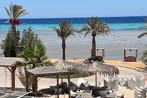 Blick auf Strandlounge mit weißen Sesseln, Palmen und Meer – exklusives Urlaubsfeeling am The Breakers Hotel in Ägypten