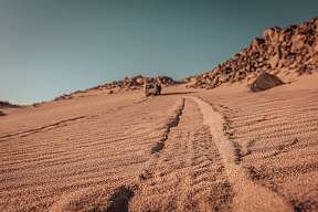 Reifenspuren im Sand führen zum Jeep in der Ferne – auf Safari-Tour in der Wüste Ägyptens mit WUNDERORTE