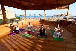 Fünf Frauen praktizieren Yoga mit Blick auf das türkisblaue Meer im offenen Holzpavillon des Hotels The Breakers in Soma Bay