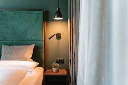Stilvolle Detailaufnahme eines Bettes mit grünem Samtkopfteil, Leselicht und Naturmaterialien – Design-Schlafzimmer im Wellnesshotel in Tirol I WUNDERORTE