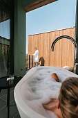 Frau liegt entspannt im Whirlpool einer modernen Suite mit Blick auf ihren Partner auf der Terrasse – Design und Privatsphäre in Südtirol bei WUNDERORTE