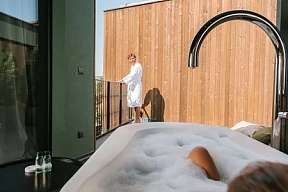 Frau liegt entspannt im Whirlpool einer modernen Suite mit Blick auf ihren Partner auf der Terrasse – Design und Privatsphäre in Südtirol bei WUNDERORTE