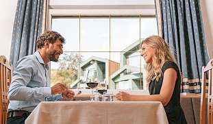 Ein Paar genießt ein stilvolles Abendessen mit Rotwein im Restaurant eines Designhotels in Kastelruth – romantische Auszeit mit Dolomitenblick I WUNDERORTE
