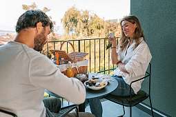 Ein Paar genießt ein entspanntes Frühstück auf der privaten Terrassensuite mit Picknickkorb und Naturblick – kulinarische Morgenruhe I WUNDERORTE