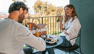 Ein Paar genießt ein entspanntes Frühstück mit Picknickkorb auf der privaten Terrasse eines Luxuschalets in Südtirol – Genuss &amp; Morgenruhe I WUNDERORTE