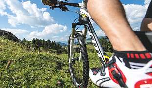 Perspektivaufnahme eines Mountainbikers mit Blick über die Sommerlandschaft der Seiser Alm – Aktivurlaub mit Dolomitenblick I WUNDERORTE