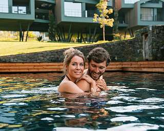 Paar genießt eine innige Auszeit im Naturpool vor modernen Designchalets in Tirol – Rückzug, Genuss und besondere Momente mit WUNDERORTE.