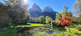 Weitläufiger Hotelgarten mit Teich, Herbstbaum und Blick auf die imposanten Dolomiten – Ruhe und Bergidylle in Tirol I WUNDERORTE