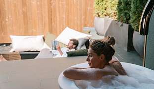 Paar genießt eine private Wellness-Auszeit im Whirlpool und modernem TerrassenHängenetz eines Design Chalet - symbolisiert ein Rückzugsort für Entspannung, Nähe und neue Energie bei WUNDERORTE