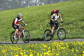 Zwei Radfahrer fahren durch blühende Wiesen auf der Seiser Alm – Aktivsein in der Natur mit Dolomitenblick I WUNDERORTE