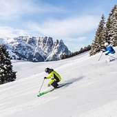 Zwei Skifahrer auf einer sonnigen Piste mit Blick auf die verschneiten Dolomiten – Winterfreude in Südtirol I WUNDERORTE