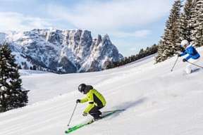 Zwei Skifahrer auf einer sonnigen Piste mit Blick auf die verschneiten Dolomiten – Winterfreude in Südtirol I WUNDERORTE