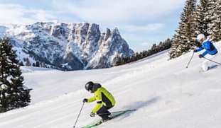 Zwei Skifahrer in voller Fahrt auf verschneiter Piste mit Panoramablick auf die Dolomiten – Wintersporturlaub in Kastelruth I WUNDERORTE