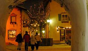 Personen spazieren durch das weihnachtlich beleuchtete Dorf Kastelruth bei Nacht – stimmungsvolle Adventzeit in den Dolomiten I WUNDERORTE