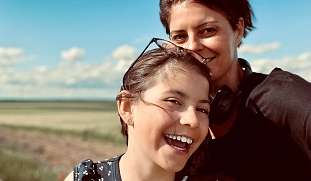 Eine Frau und ein Mädchen lächeln gemeinsam in die Kamera, vor ihnen eine weite Naturkulisse – Symbol für Nähe, Vertrauen und persönliche Begleitung bei WUNDERORTE.