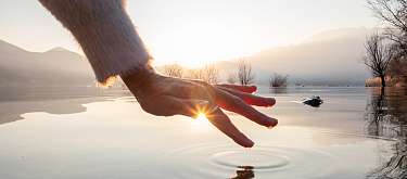 WUNDERORTE - achtsames Reisen. Hand über ruhigem Wasser am See. 