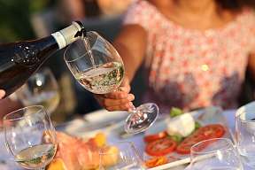 Ein Glas Weißwein wird im Sonnenlicht auf einer Terrasse eingeschenkt – entspannte Atmosphäre mit Antipasti und Sommergenuss bei WUNDERORTE