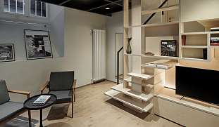 Design-Wohnbereich im Ferienhaus mit gemütlicher Sitzecke, Bücherwand, Galerieebene und offener Treppe – stilvolle Ferienwohnung in Südtirol bei WUNDERORTE