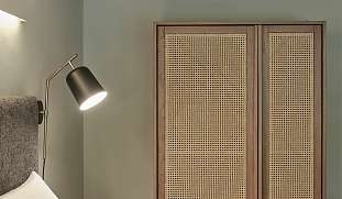 Detailaufnahme eines Designbetts mit Rattanschrank, Leselampe und Naturfarben im PARCLOFT Meran I WUNDERORTE