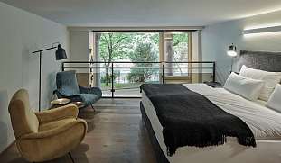 Offener Schlafbereich im Designloft PARCLOFT Meran mit großen Fenstern, Lounge-Sesseln und Blick in den Park I WUNDERORTE