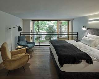 Offener Schlafbereich im Designloft PARCLOFT Meran mit großen Fenstern, Lounge-Sesseln und Blick in den Park I WUNDERORTE