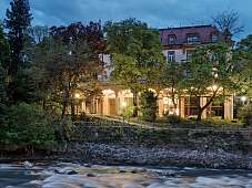 Beleuchtetes Stadtpalais am Fluss in Meran bei Abenddämmerung – Design-Ferienunterkunft mit historischem Flair, umgeben von Natur und Licht | WUNDERORTE