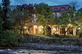 Beleuchtetes Stadtpalais am Fluss in Meran bei Abenddämmerung – Design-Ferienunterkunft mit historischem Flair, umgeben von Natur und Licht | WUNDERORTE